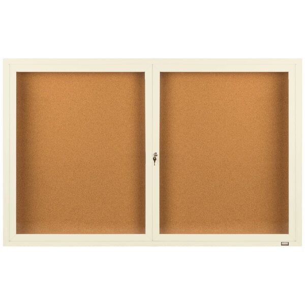 An Aarco ivory bulletin board cabinet with glass doors on a white background.
