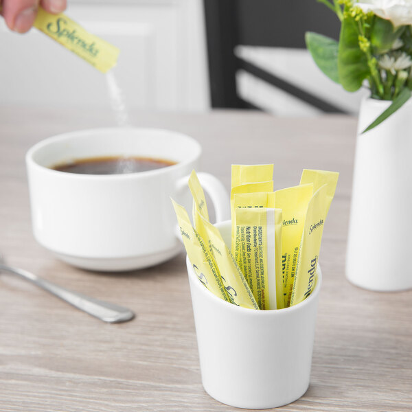 A person pouring sugar into a cup of coffee using a Schonwald white porcelain sugar stick holder.