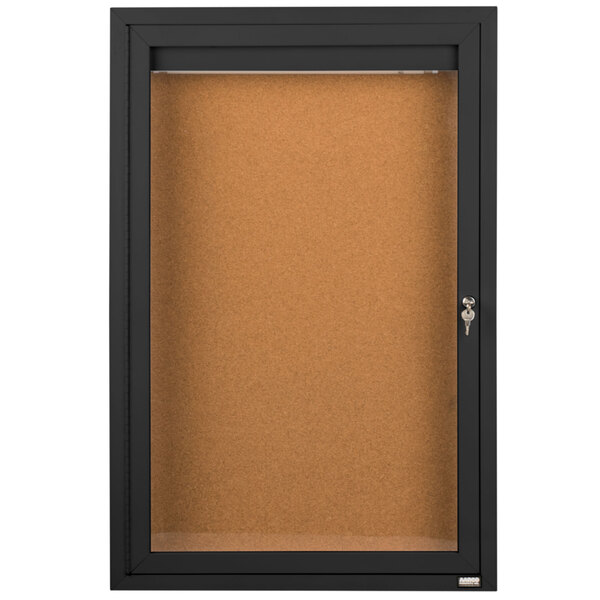 A black indoor lighted bulletin board cabinet with a cork board and a key.