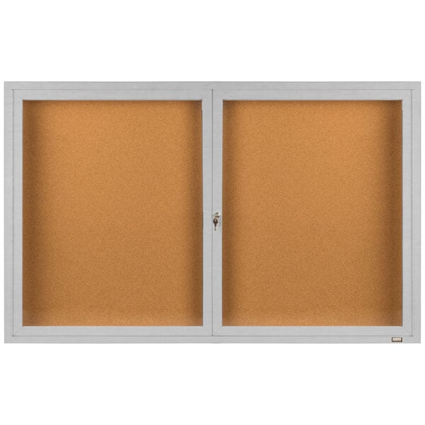 An Aarco enclosed bulletin board cabinet with a satin anodized finish and white framed bulletin board.