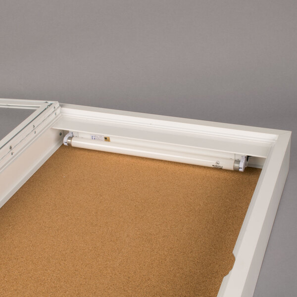 A white rectangular cabinet with a glass door and a cork bulletin board inside.