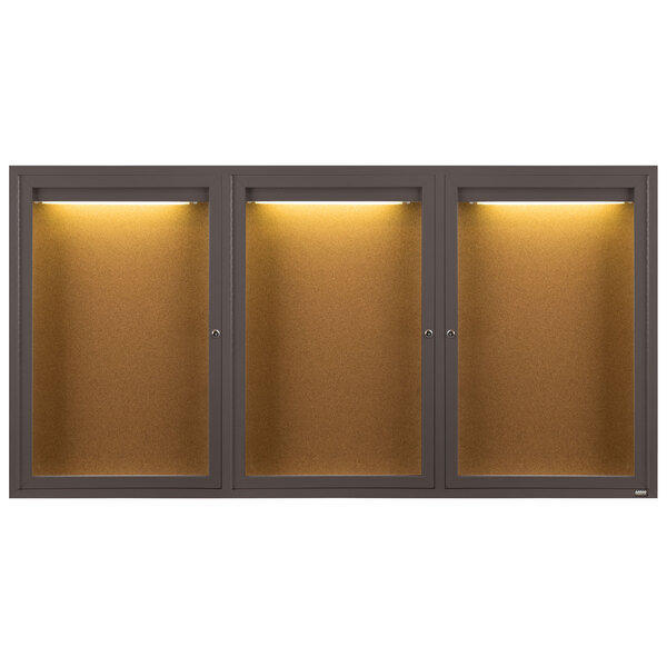 An Aarco bronze anodized indoor bulletin board cabinet with three glass doors and lights.