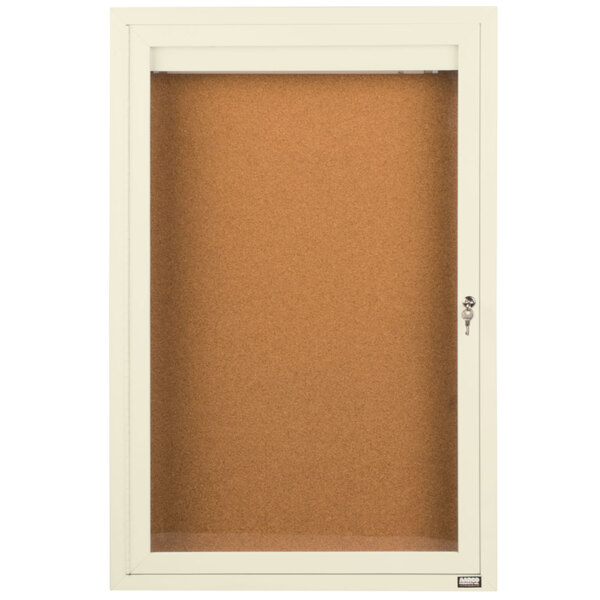 An ivory Aarco enclosed bulletin board cabinet with a cork board inside and a key lock.