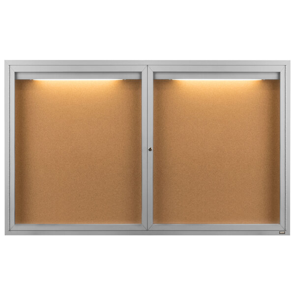 An Aarco satin anodized cork board cabinet with lights on inside.