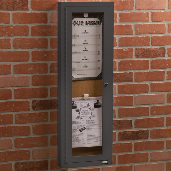 An Aarco bronze indoor bulletin board cabinet with a menu inside on a bulletin board.