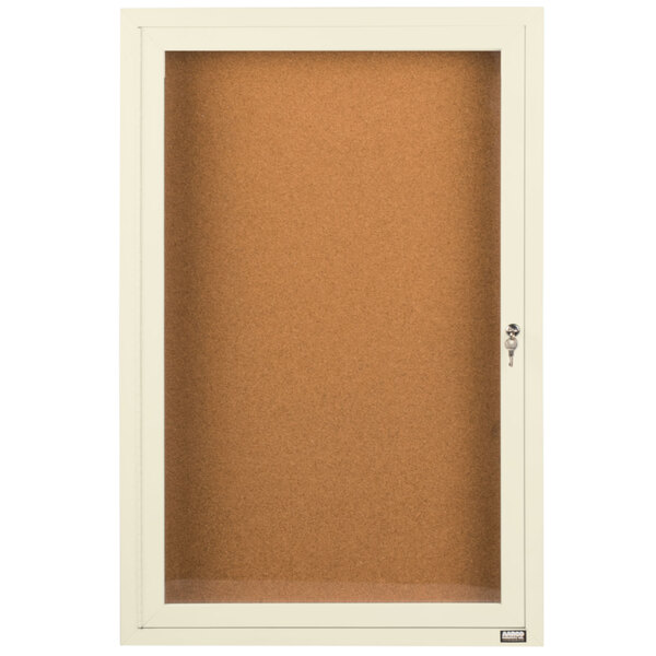 An ivory Aarco enclosed bulletin board cabinet with a door.