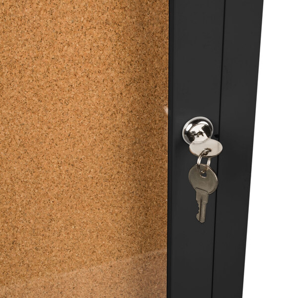 A black metal Aarco bulletin board cabinet with a key in the lock.
