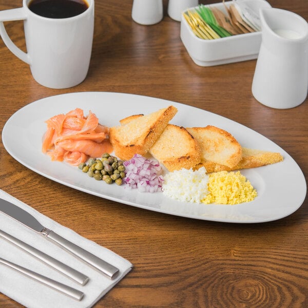 A Schonwald white porcelain oval platter with food, a knife, and a fork on it.