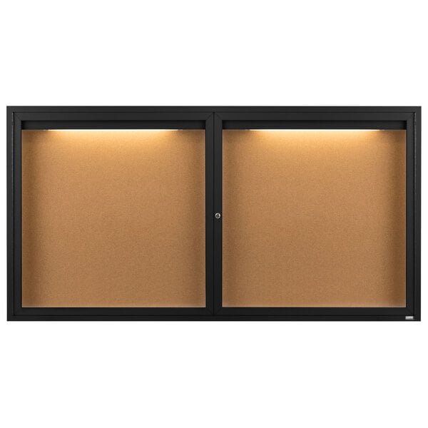 A black Aarco enclosed bulletin board cabinet with lights on.