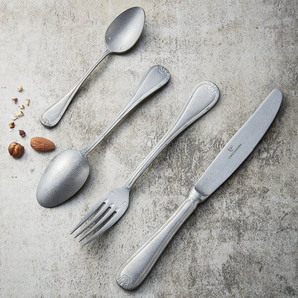 A Chef & Sommelier stainless steel dinner knife on a table with silverware and nuts.