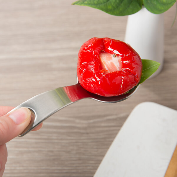 A hand holding a Schonwald tapas spoon with a red pepper on it.