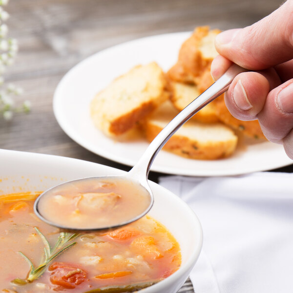 A person holding a Chef & Sommelier stainless steel soup spoon over a bowl of soup.