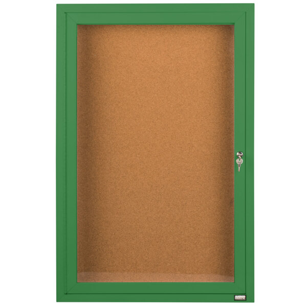 A green framed Aarco indoor bulletin board cabinet with a cork board and a glass door with a key.