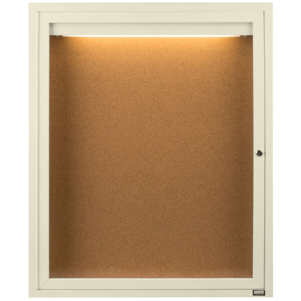 An ivory Aarco enclosed bulletin board cabinet with a light on it.