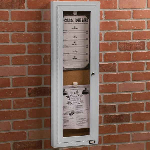 An Aarco satin anodized indoor bulletin board cabinet with a paper menu inside.