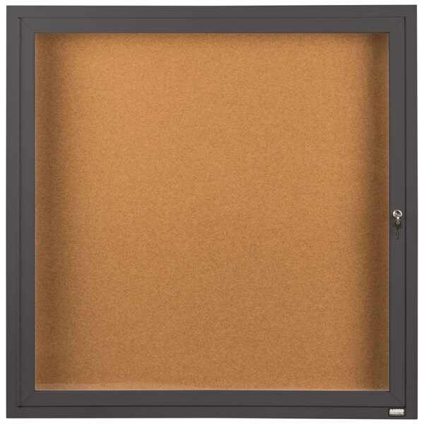 An Aarco bronze bulletin board cabinet with 1 door and a key.