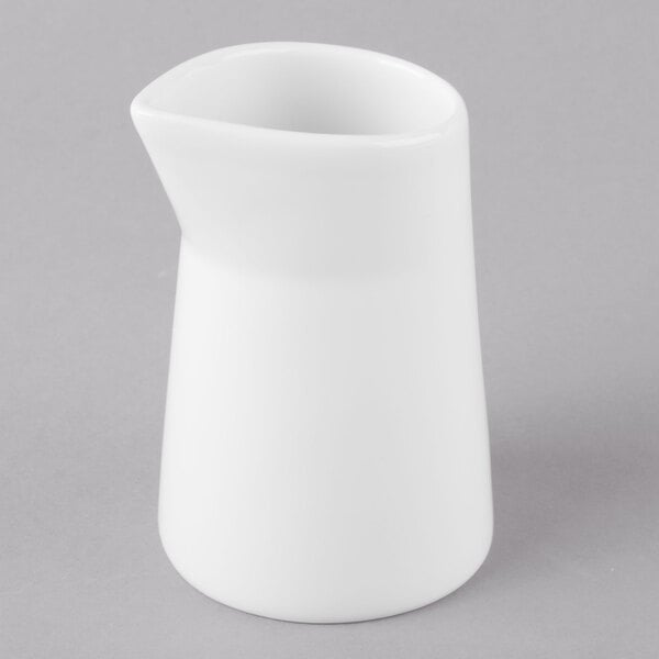A Schonwald white porcelain creamer pitcher with a white handle on a gray surface.