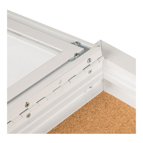 A close-up view of the corner of a white metal-framed bulletin board cabinet with a corkboard interior and a hinged door.