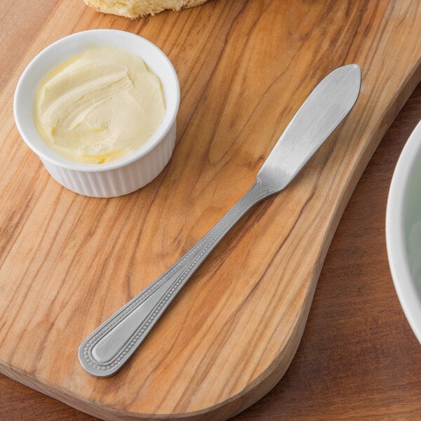 Butter knife on wooden cutting board with ramekin of butter