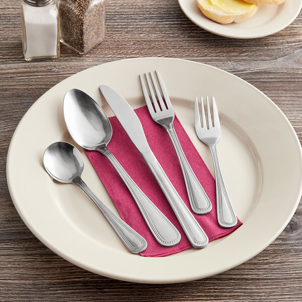 A Choice Milton stainless steel butter knife on a white plate with silverware.