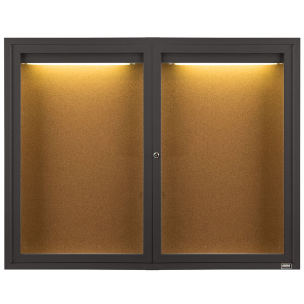 A bronze Aarco bulletin board cabinet with two glass doors and two lights.