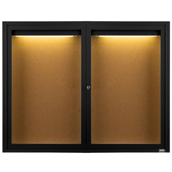 A black Aarco bulletin board cabinet with two glass doors and a light inside.