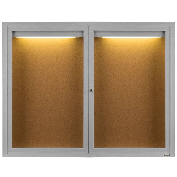 A white Aarco bulletin board cabinet with two lighted doors.