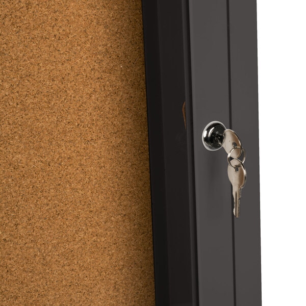 A bronze Aarco bulletin board cabinet with a key in the lock.