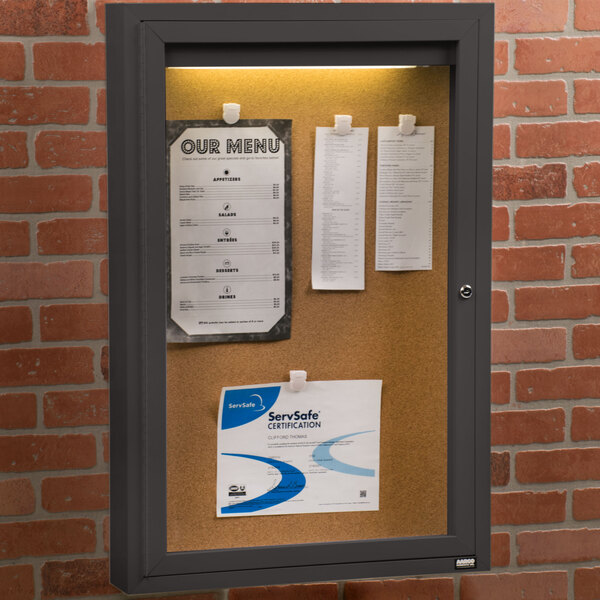 An Aarco bronze indoor lighted bulletin board cabinet with a notice attached to it.