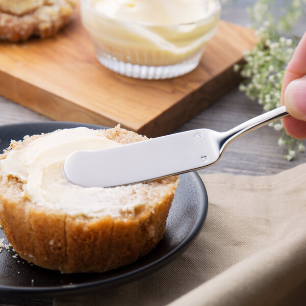A person using a Chef & Sommelier stainless steel butter spreader to spread butter on bread.