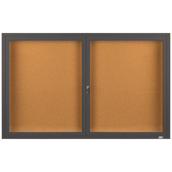 A brown rectangular Aarco bulletin board cabinet with two black enclosed glass doors.