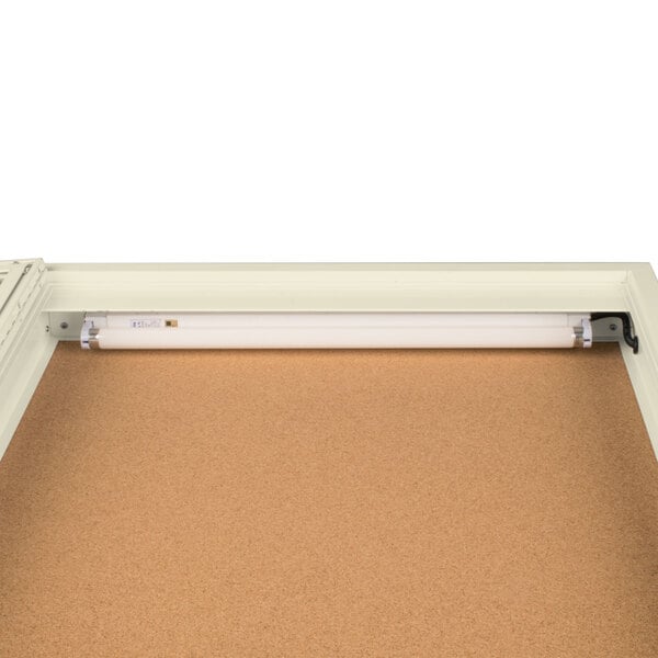 An Aarco ivory bulletin board cabinet with a light inside.