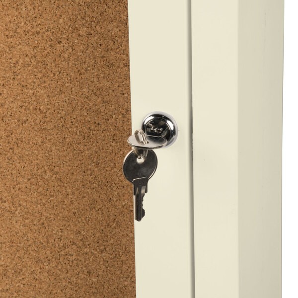 The inside of an ivory Aarco bulletin board cabinet with a key in the lock.