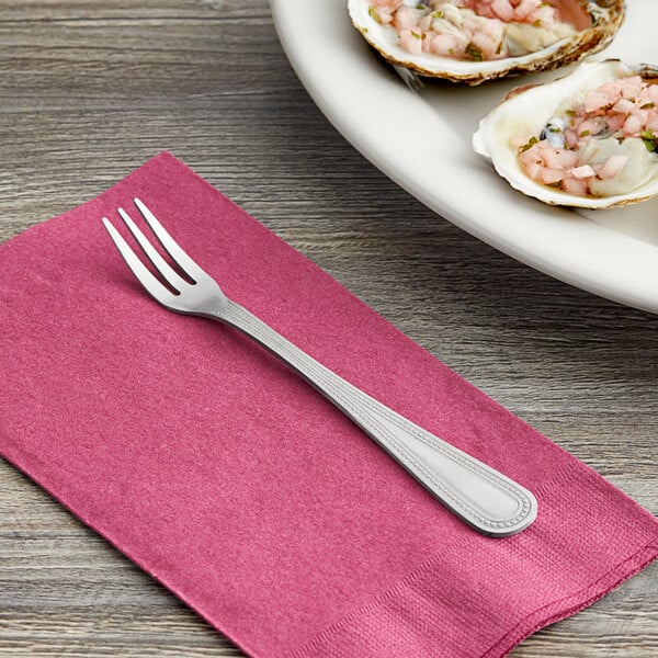 A Choice Milton stainless steel cocktail/oyster fork on a pink napkin next to a plate of oysters.