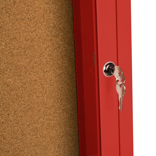 A red indoor bulletin board cabinet with a key in the lock.