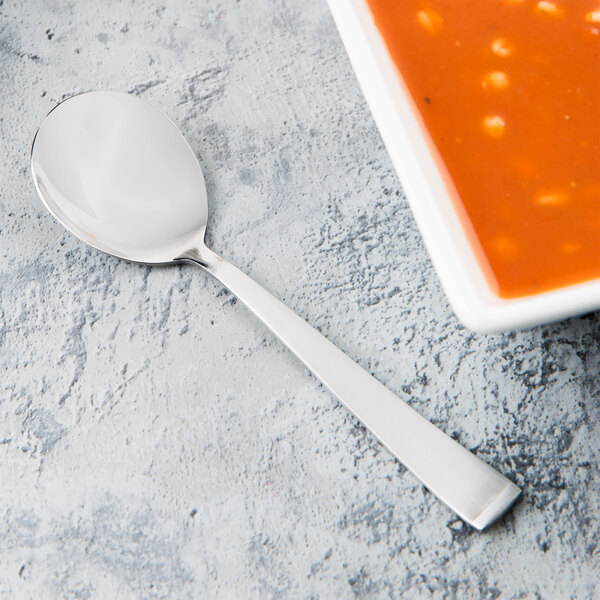 A Libbey stainless steel bouillon spoon next to a bowl of soup.