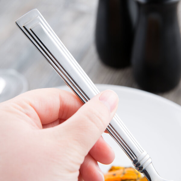 A hand holding a Libbey stainless steel dinner fork over a white plate of food.