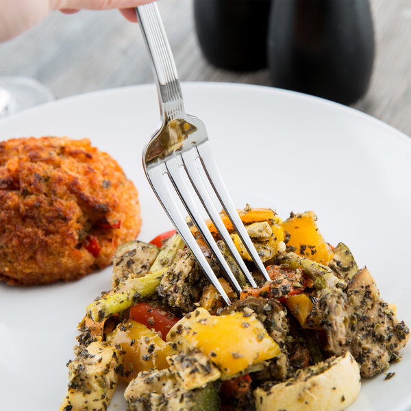 A hand holding a Libbey stainless steel dinner fork over a plate of food.