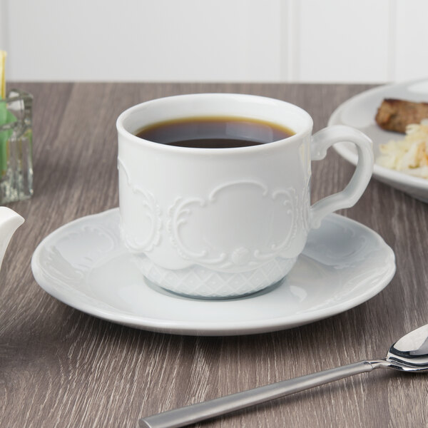 A white Schonwald stacking cup of coffee on a table with food on a plate.
