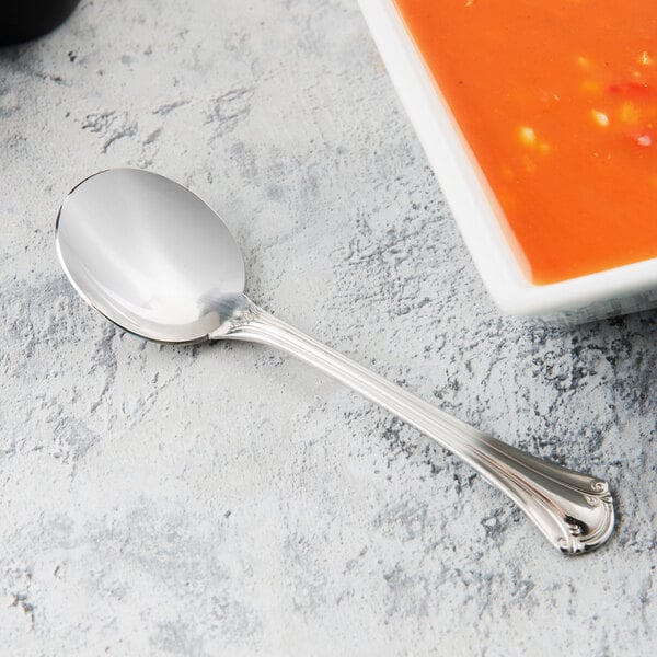 A World Tableware stainless steel bouillon spoon next to a bowl of soup.