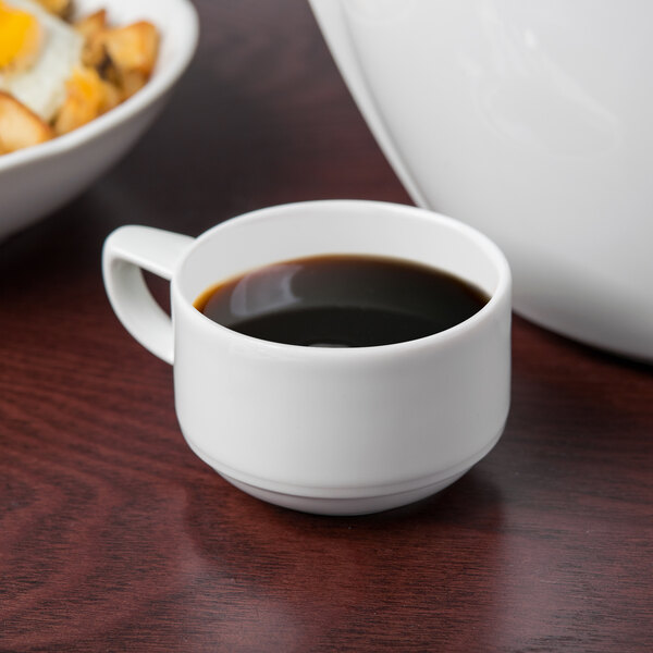 A Schonwald white porcelain espresso cup filled with coffee on a table next to a bowl of food.