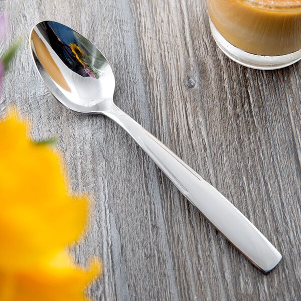 A Libbey stainless steel teaspoon on a table next to a cup of coffee.