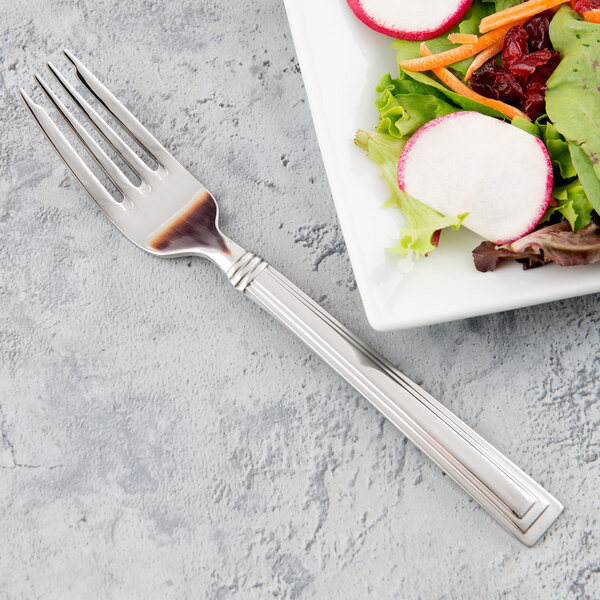 A Libbey stainless steel salad fork next to a plate of salad.