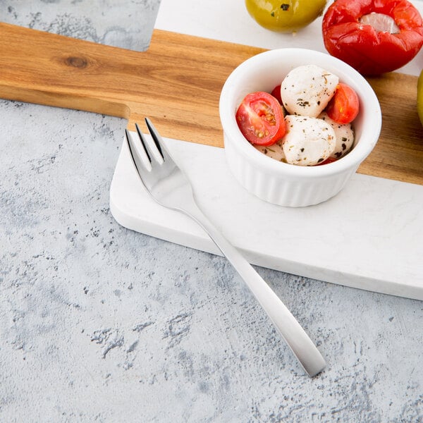 A Libbey stainless steel cocktail fork in a bowl of tomatoes and cheese on a cutting board.