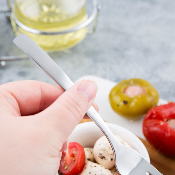 A person's hand holding a Libbey stainless steel cocktail fork over a bowl of food.