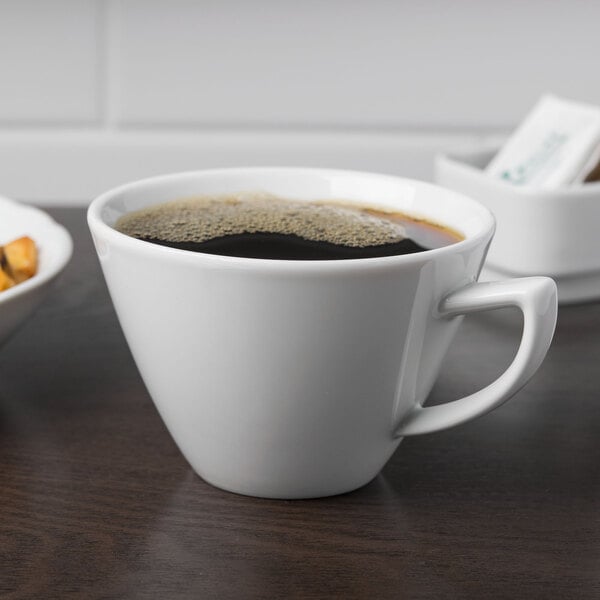 A Schonwald white porcelain cup of coffee on a table with food.