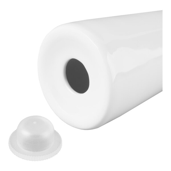 A white cylindrical object with a hole at one end and a separate small, round, translucent cap placed nearby.