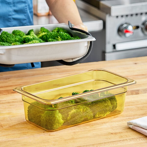 A woman's hand holding a Carlisle amber plastic food pan with broccoli inside.