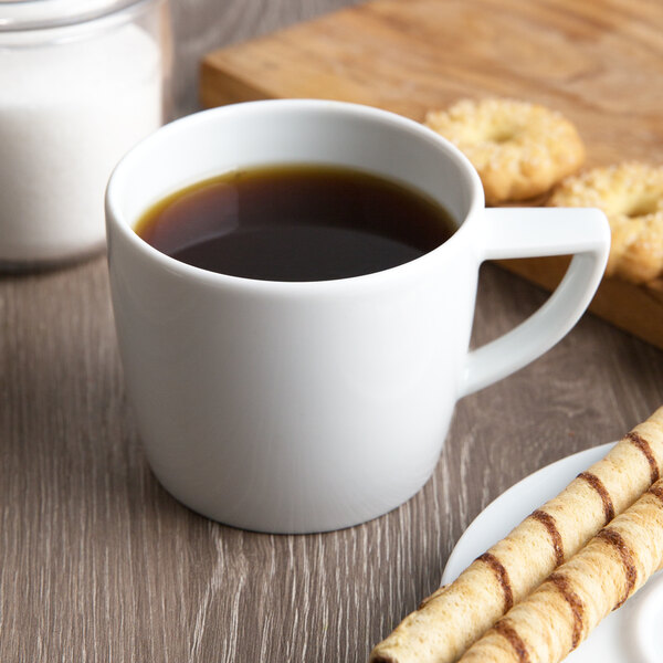 A Schonwald white porcelain cup of coffee and cookies on a table.