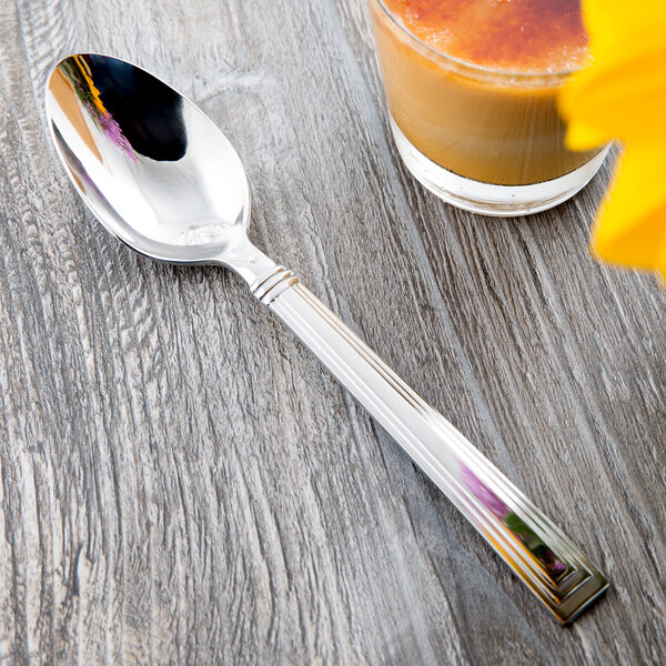 A Libbey stainless steel dessert spoon in a glass of liquid on a table.